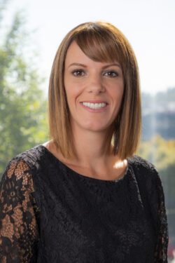 photo of woman in a black top, shoulder-length brown hair with bangs, and a natural background with green leafy trees; photo is of Lori Robbin, newly appointed Managing Principal at BCRA